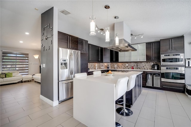 kitchen with pendant lighting, island exhaust hood, tasteful backsplash, stainless steel appliances, and light countertops