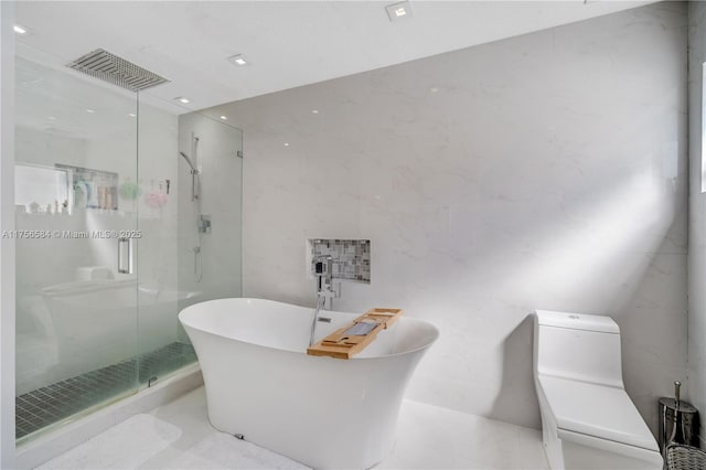 bathroom featuring visible vents, toilet, a stall shower, a freestanding tub, and tile walls