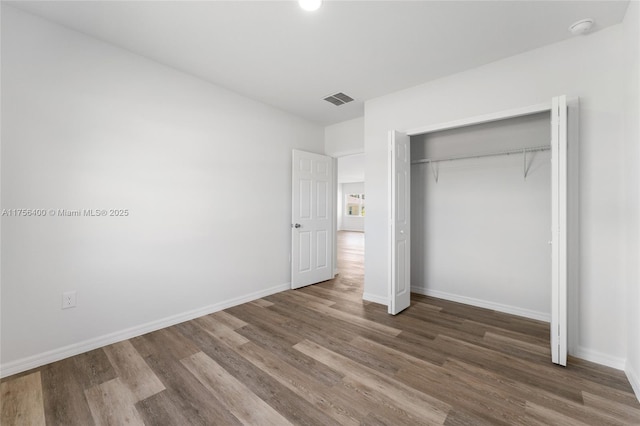 unfurnished bedroom with a closet, visible vents, baseboards, and wood finished floors