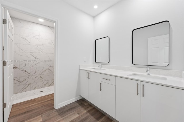 full bathroom featuring wood finished floors, a sink, baseboards, tiled shower, and double vanity