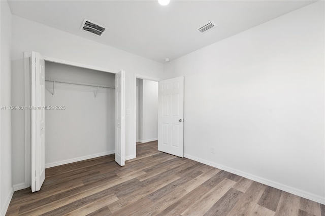 unfurnished bedroom featuring a closet, visible vents, baseboards, and wood finished floors