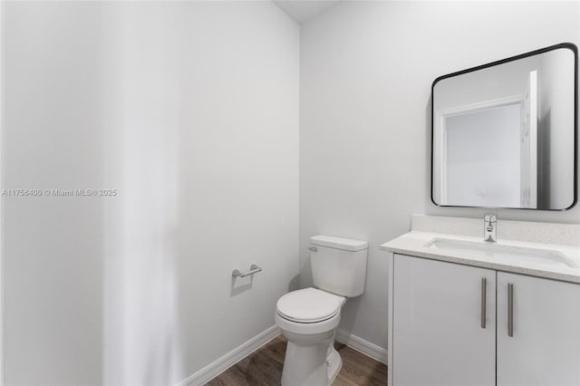 half bathroom with vanity, wood finished floors, toilet, and baseboards