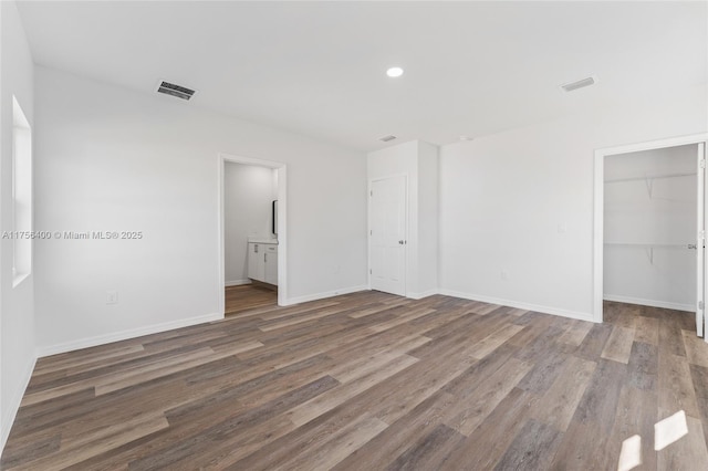 unfurnished bedroom featuring wood finished floors, visible vents, baseboards, a spacious closet, and a closet