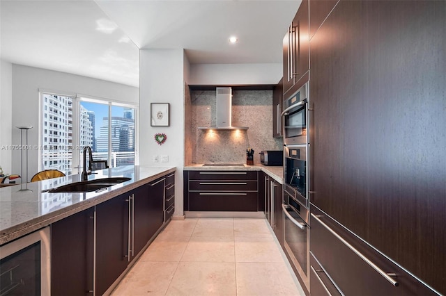 kitchen featuring light tile patterned floors, oven, beverage cooler, a sink, and wall chimney range hood