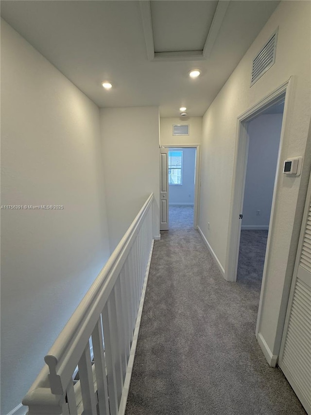 hall featuring carpet floors, attic access, visible vents, and a decorative wall