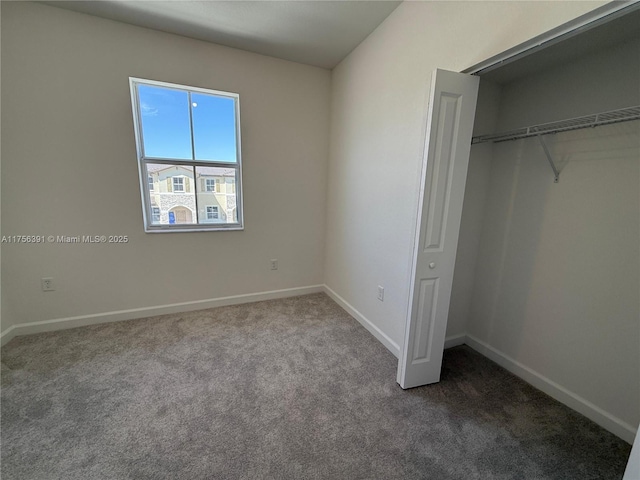 unfurnished bedroom featuring baseboards, dark carpet, and a closet