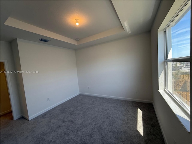 spare room featuring carpet floors, a raised ceiling, visible vents, and baseboards