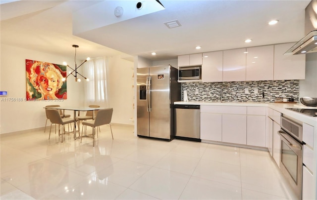 kitchen with wall chimney exhaust hood, appliances with stainless steel finishes, a sink, white cabinetry, and backsplash