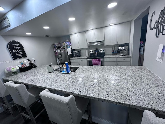 kitchen featuring a breakfast bar, recessed lighting, appliances with stainless steel finishes, a peninsula, and under cabinet range hood