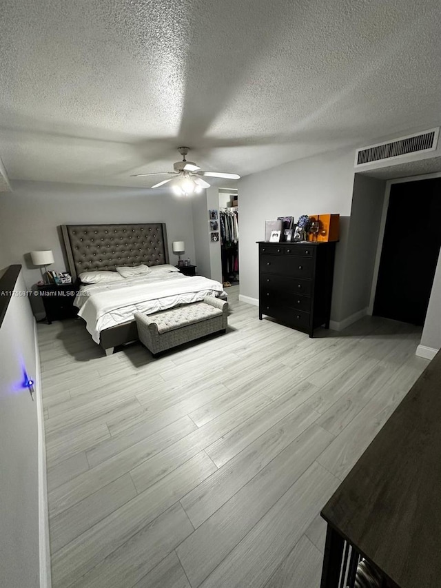 bedroom featuring a textured ceiling, visible vents, a spacious closet, a closet, and light wood finished floors