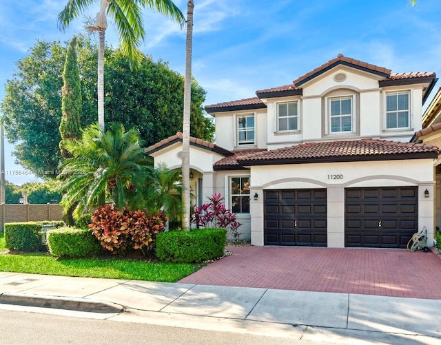 mediterranean / spanish-style home with decorative driveway, fence, a tile roof, and stucco siding