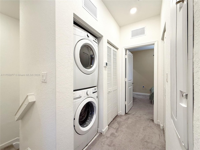 laundry area featuring stacked washer / dryer, baseboards, visible vents, and carpet