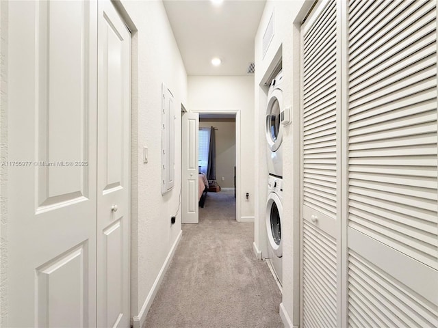 laundry area featuring a textured wall, light carpet, laundry area, baseboards, and stacked washing maching and dryer