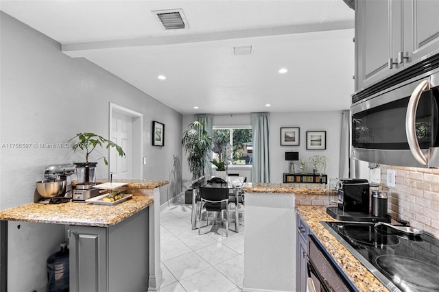 kitchen with stainless steel microwave, gray cabinets, a peninsula, visible vents, and stovetop