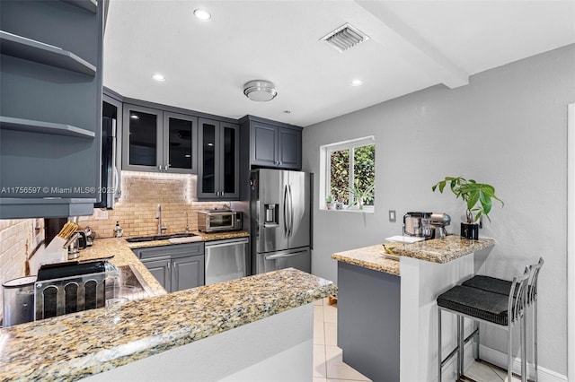 kitchen featuring a peninsula, backsplash, visible vents, stainless steel appliances, and a sink