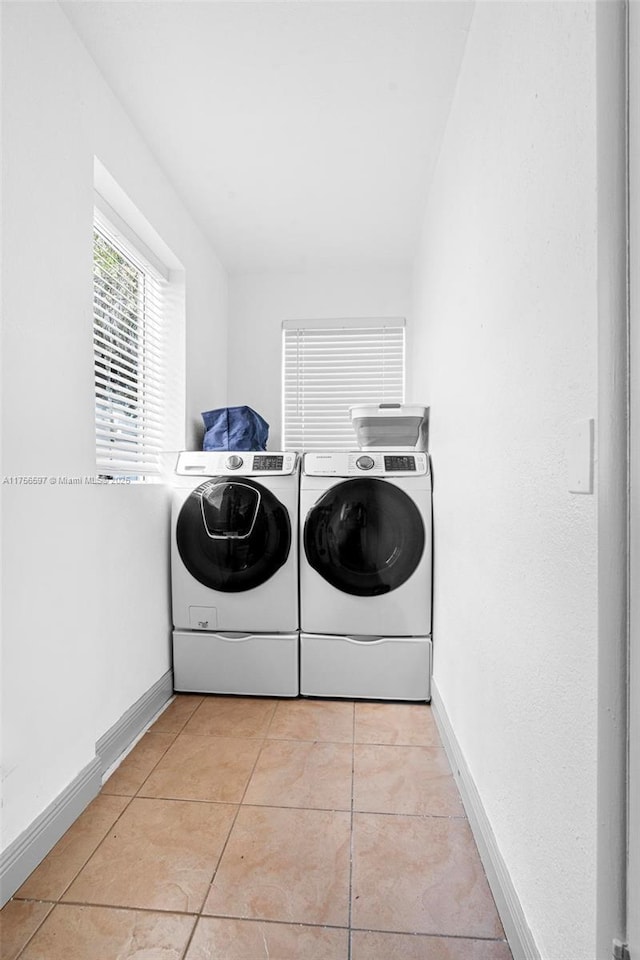 clothes washing area with independent washer and dryer, light tile patterned floors, laundry area, and baseboards