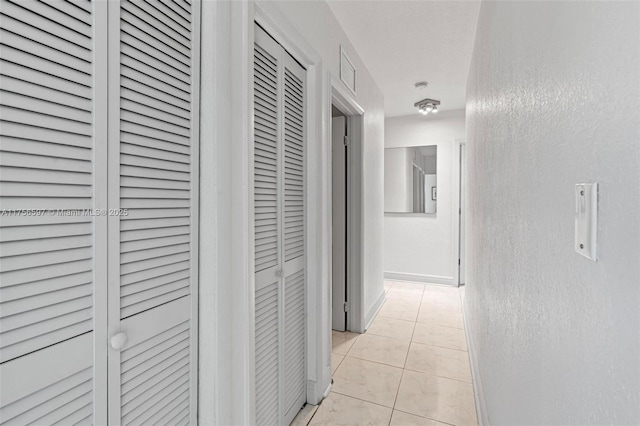 hall with a textured wall, light tile patterned floors, visible vents, and baseboards