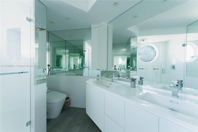 bathroom featuring double vanity, a sink, toilet, and wood finished floors