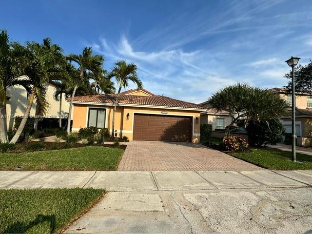 view of front of property with stucco siding, a tiled roof, an attached garage, decorative driveway, and a front yard