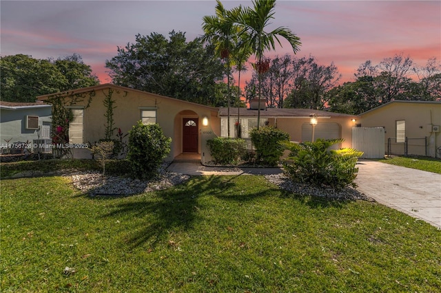 mediterranean / spanish-style home with an attached garage, fence, decorative driveway, a yard, and stucco siding