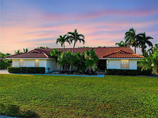 ranch-style home featuring a tiled roof, a lawn, and stucco siding