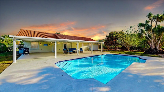 pool at dusk with a patio area, an outdoor pool, and an outdoor hangout area