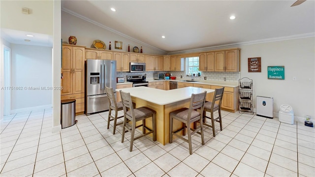 kitchen featuring a breakfast bar area, a sink, light countertops, ornamental molding, and appliances with stainless steel finishes