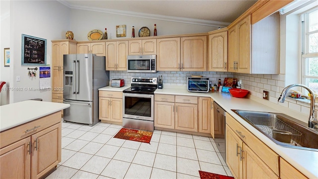 kitchen featuring lofted ceiling, appliances with stainless steel finishes, crown molding, light brown cabinetry, and a sink