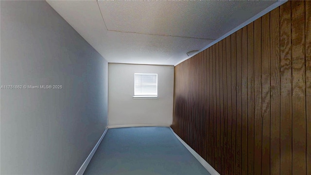 hall featuring carpet floors, wood walls, baseboards, and a textured ceiling