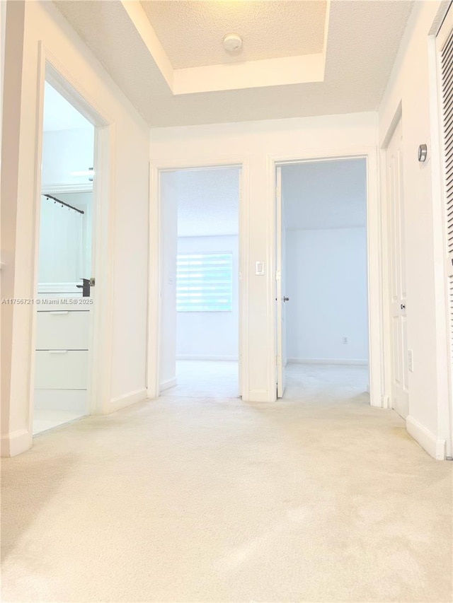 hallway featuring light carpet, baseboards, and a raised ceiling