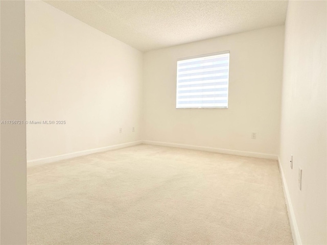 spare room with baseboards, a textured ceiling, and light colored carpet