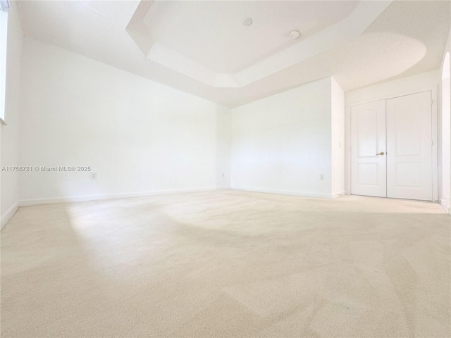 unfurnished room with baseboards, a tray ceiling, and light colored carpet