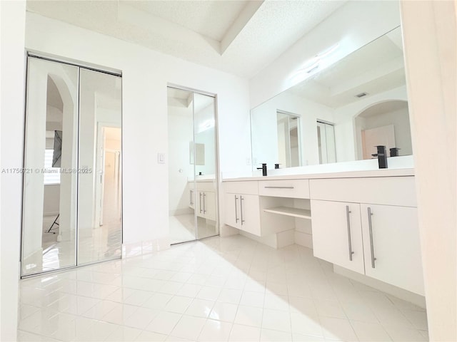 bathroom with a textured ceiling, tile patterned flooring, a sink, double vanity, and a raised ceiling