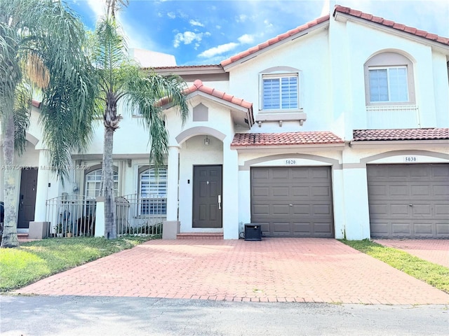 mediterranean / spanish home with a garage, a tiled roof, decorative driveway, and stucco siding