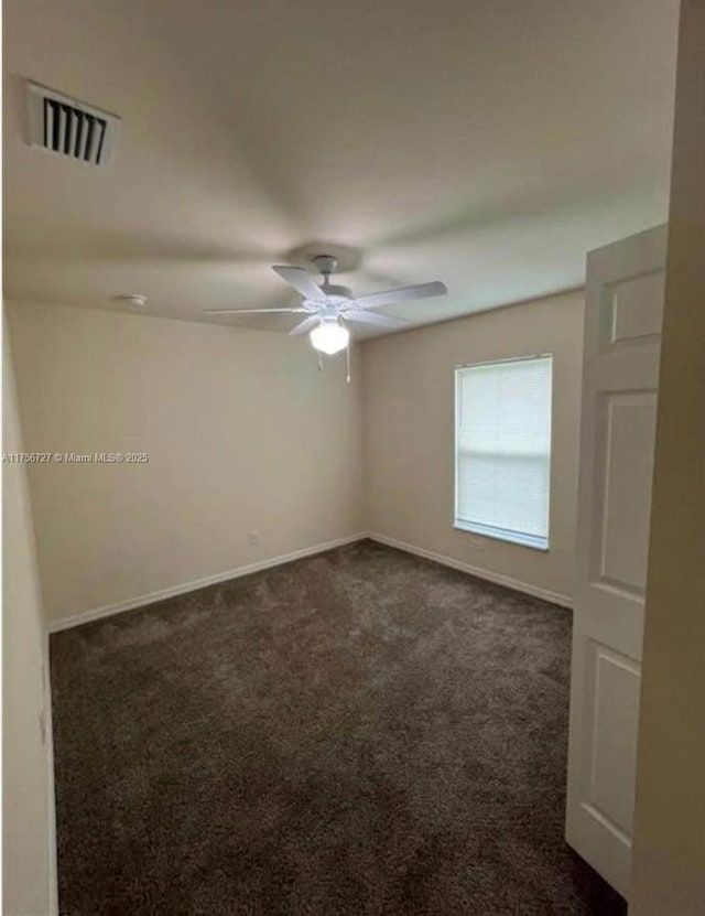 empty room featuring a ceiling fan, visible vents, dark carpet, and baseboards