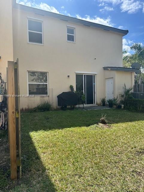 rear view of house with a yard, fence, and stucco siding