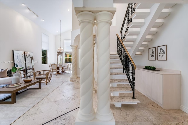 stairs featuring decorative columns, rail lighting, a high ceiling, stone tile flooring, and a notable chandelier