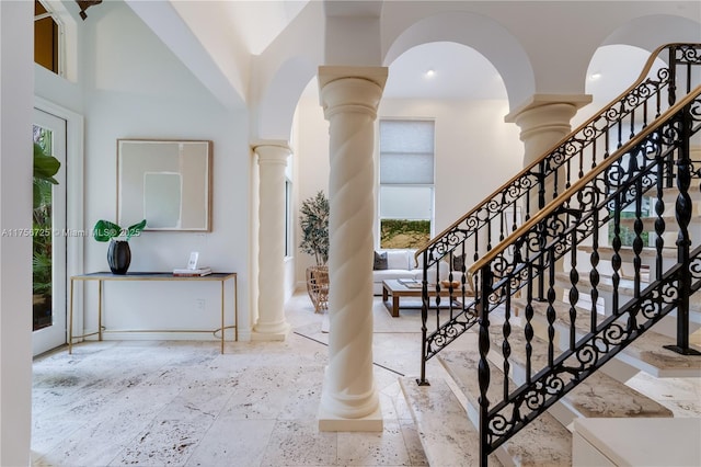 foyer with a towering ceiling, decorative columns, and stone tile floors