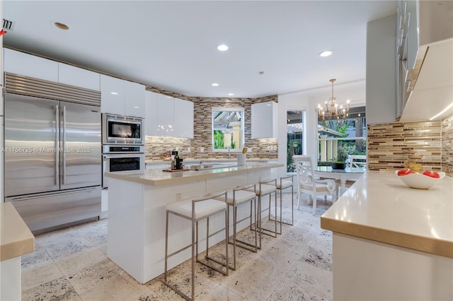 kitchen featuring built in appliances, recessed lighting, white cabinets, backsplash, and a kitchen bar