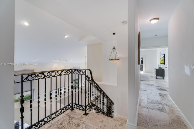 corridor featuring baseboards, an upstairs landing, visible vents, and stone tile floors