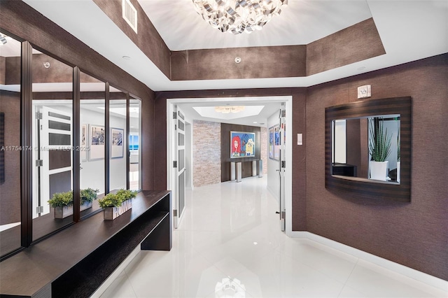 hall with tile patterned floors, visible vents, baseboards, and a notable chandelier