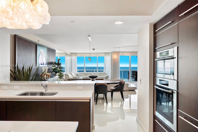 kitchen with a sink, open floor plan, dark brown cabinetry, double oven, and light countertops