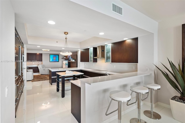 kitchen featuring visible vents, dark brown cabinets, light tile patterned floors, a kitchen breakfast bar, and wall chimney exhaust hood