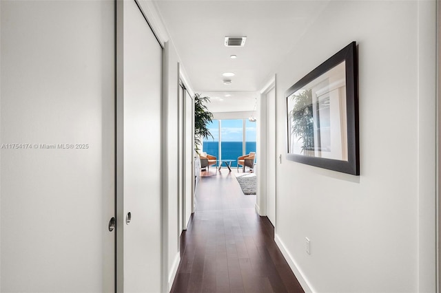 hall featuring visible vents, baseboards, dark wood-type flooring, and a water view