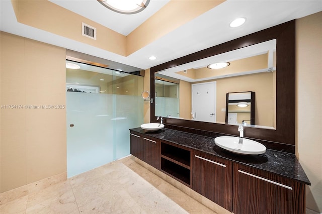 full bath featuring double vanity, visible vents, a walk in shower, and a sink