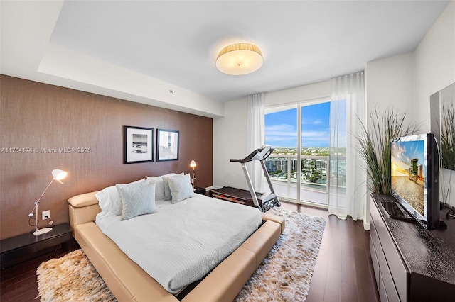 bedroom featuring dark wood-style floors, an accent wall, and access to outside