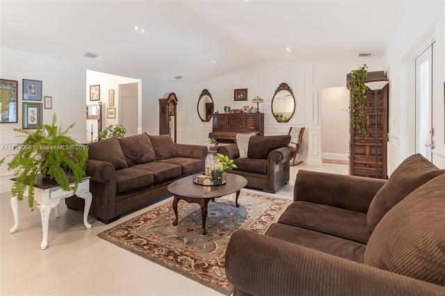 living room featuring lofted ceiling, visible vents, and a decorative wall