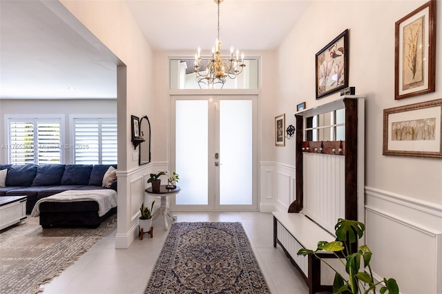 tiled entrance foyer featuring a wainscoted wall, french doors, a decorative wall, and an inviting chandelier