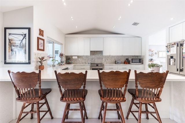 kitchen featuring visible vents, decorative backsplash, a peninsula, stainless steel appliances, and light countertops