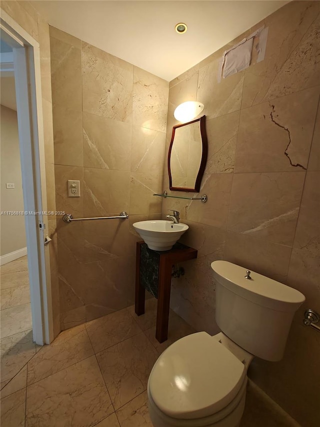 half bathroom featuring toilet, a sink, and tile walls